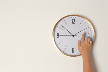Woman touching clock on light wall, space for text. Time management