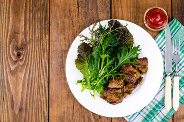 Slices of fried liver, green leaves of salads