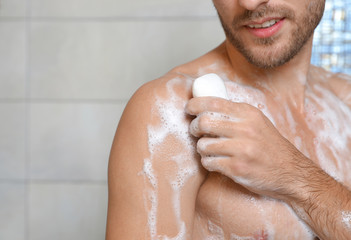 Young man taking shower with soap in bathroom, closeup. Space for text