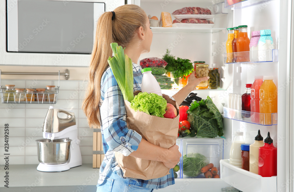 Wall mural Woman putting products into refrigerator in kitchen