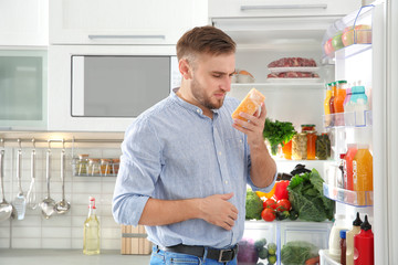 Man feeling bad smell from stale cheese near refrigerator at home - obrazy, fototapety, plakaty