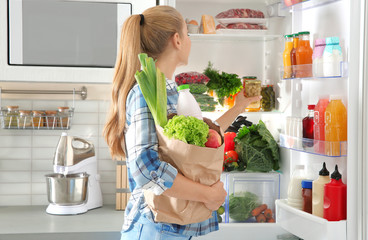 Woman putting products into refrigerator in kitchen
