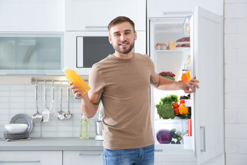 Man with bottle of juice standing near open refrigerator in kitchen