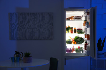 Stylish kitchen interior with refrigerator full of products at night