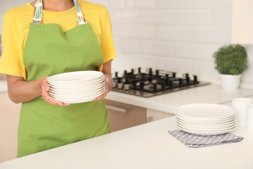 Woman holding stack of clean dishes in kitchen