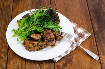 Slices of fried liver, green leaves of salads