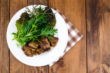 Slices of fried liver, green leaves of salads