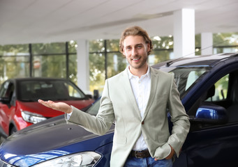 Fototapeta na wymiar Young man near new car in modern auto dealership