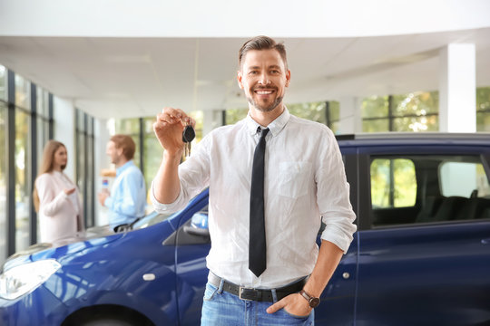 Salesman with car keys in modern auto dealership