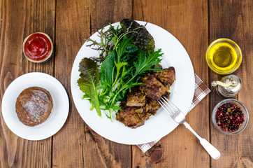 Slices of fried liver, green leaves of salads