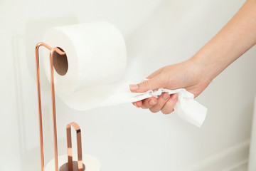 Woman taking toilet paper from roll holder in bathroom, closeup