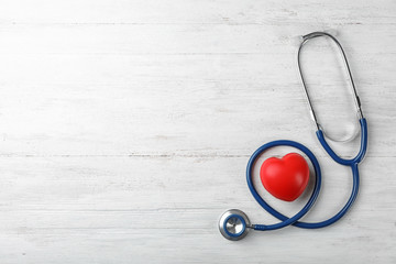 Stethoscope for checking pulse and red heart on light background, top view. Space for text