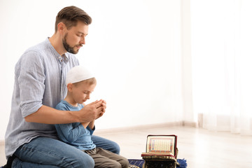 Muslim man and his son praying together indoors. Space for text