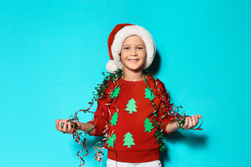 Cute little boy in handmade Christmas sweater and hat with streamers on color background