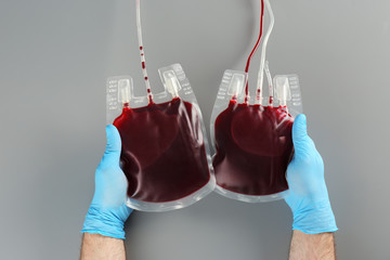 Doctor in gloves holding blood packs on gray background, top view. Donation day