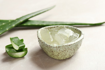 Bowl with aloe vera gel and fresh leaves on gray table