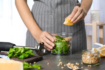 Woman making basil pesto sauce at kitchen table