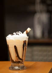 Coffee latte with wipped cream served in a small glass with sweet stick and chocolate topping