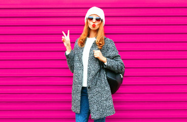 Cool girl blowing red lips sends an air kiss posing on colorful pink wall background