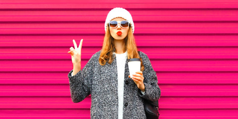 Fashion and people concept - cool stylish woman blowing red lips sends an air kiss on colorful pink wall background