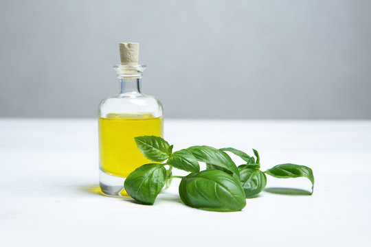 Glass bottle of oil and basil leaves on light table. Space for text