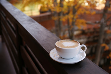 Hot cozy drink in cup on wooden railing at balcony. Space for text