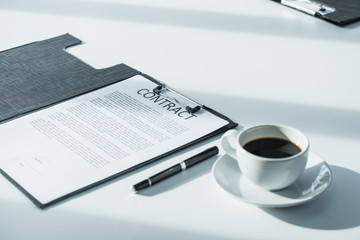 Close up business contract paper on meeting room table with pen and coffee cup in sun light shadow with green plant at office,business agreement concept.
