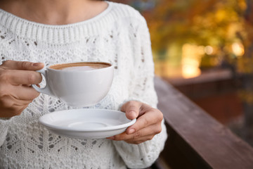 Woman in warm sweater holding cup with hot cozy drink on balcony