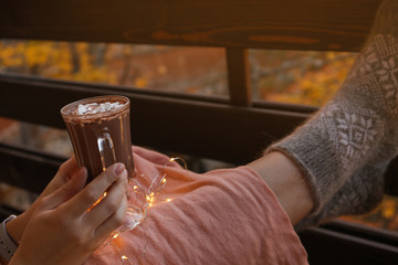 Woman in warm woolen socks with cup of hot cozy drink on balcony