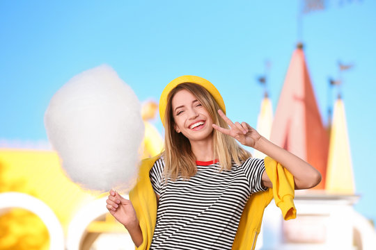 Young cheerful woman having fun with  cotton candy in amusement park