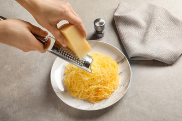 Woman grating cheese onto cooked spaghetti squash on table, closeup