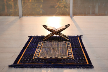 Rehal with open Quran on Muslim prayer rug indoors © New Africa