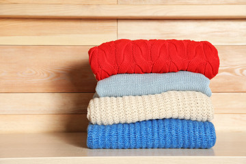Stack of winter clothes against wooden background. Space for text