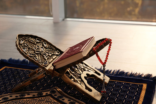 Rehal with Quran and Muslim prayer beads on rug indoors