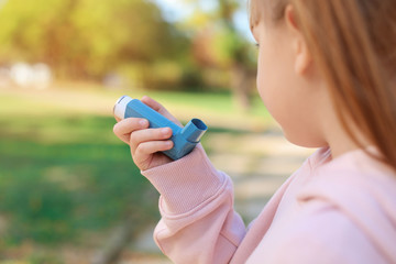 Little girl using asthma inhaler outdoors. Health care - obrazy, fototapety, plakaty