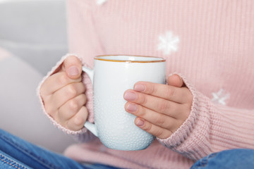Fototapeta na wymiar Young woman in warm sweater holding cup of hot drink, closeup