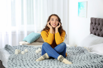Young beautiful woman in warm sweater on bed at home