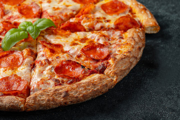 Tasty pepperoni pizza and cooking ingredients tomatoes basil on black concrete background