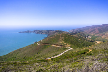 Beautiful views of the green hills of Marin Headlands crossed by a winding road; the Pacific Ocean coastline in the background; north San Francisco bay area, California