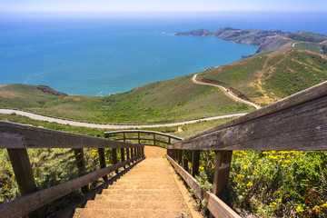 Fototapeta na wymiar Stairs descending from the top of Hawk Hill; beautiful views of the green hills and shoreline of Marin Headlands in the background; north San Francisco bay area, California
