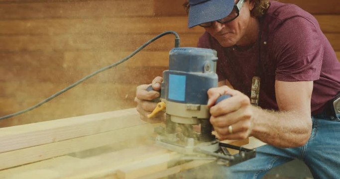 Skilled carpenter spraying lots of saw dust while using router at construction site