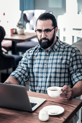 Bearded writer. Bearded writer wearing glasses feeling serious while checking his article for magazine