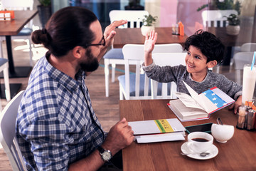 Class with tutor. Smiling dark-haired boy feeling interested enjoying class with tutor sitting in cafeteria