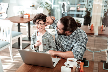 Glasses for son. Dark-haired bearded father having fun with his cute handsome son putting his glasses on him