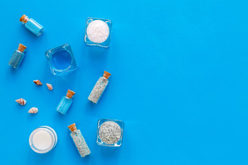 Dead sea cosmetics layout. Sea salt in bottles and bowls near small shells on blue background top view copy space