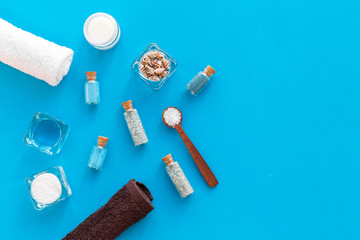Sea salt for spa and aroma spa cosmetics near towel and shells on blue background top view copy space