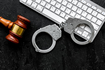 Arrest of a hacker for cyber fraud concept. Handcuff near keyboard and judge gavel on black...