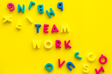 Teamwork training concept. Text teamwork lined with colored letters near toy letters on yellow background top view copy space