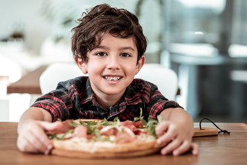 Pizza with father. Cute dark-haired son feeling excited eating pizza with his bearded caring father