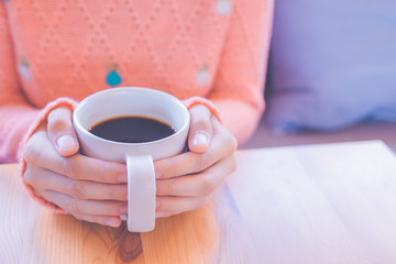 Woman hand in warm  sweater holding a cup of coffee.